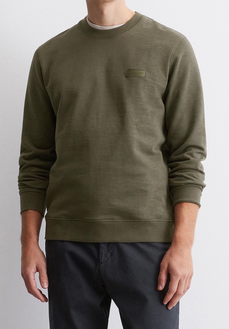 Oliwkowa bluza wykonana z miękkiego materiału, z okrągłym dekoltem, ściągaczami na rękawach i małą naszywką z logo na piersi.