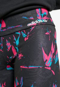 Svarta atletiska leggings med ett djärvt mönster av rosa och turkosa abstrakta former. Midjan visar Adidas-logotypen i vitt.