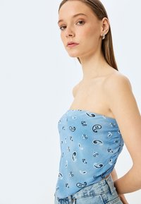 Mouwloze lichtblauwe top met paisley- en bloemenpatronen, gemaakt van een gladde stof. Geplooide stofdetails aan de zijkant.