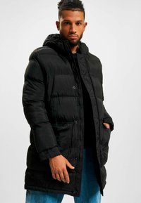 Geacă puffer din nylon negru, cu glugă, nasturi snap și buzunare. Exterior texturat cu un model matlasat care oferă izolație.
