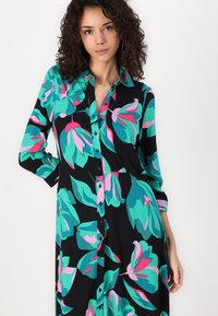 Robe chemise à motifs floraux en noir, avec de grandes fleurs teal et roses, des manches longues et un col avec des boutons centraux.
