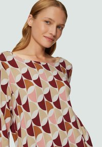 Langsleeve top in een zachte stof met een geometrisch patroon van kastanjebruine, roze, beige en bruine vormen op een lichte achtergrond.