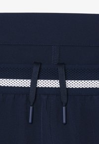 Primer plano de una cinturilla azul marino con una raya de malla blanca y dos extremos de cordón azul oscuro sobre textura de tela.