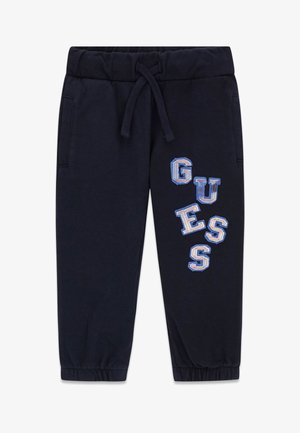 Pantaloni sportivi blu navy con vita e polsini elasticizzati, tasche frontali e scritta "GUESS" in blu e bianco sulla gamba destra.
