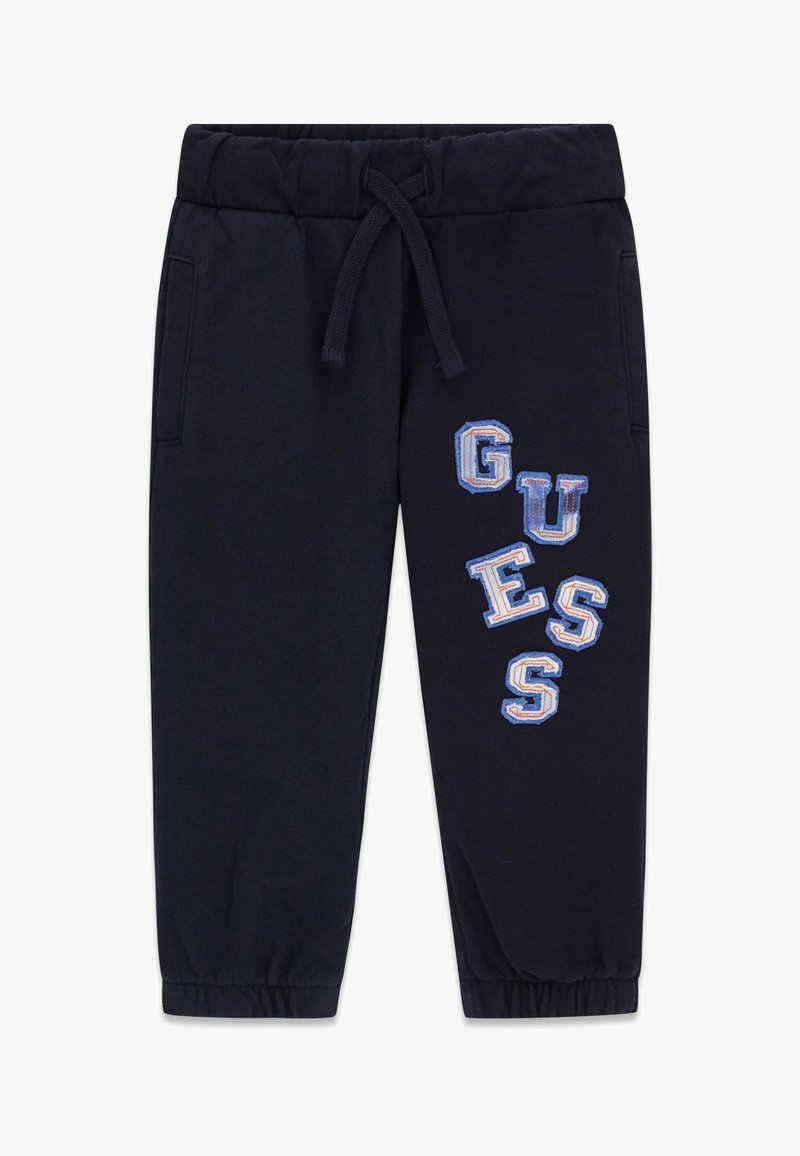 Pantalon de survêtement bleu marine avec taille et poignets élastiques, poches avant, et l'inscription "GUESS" en bleu et blanc sur la jambe droite.