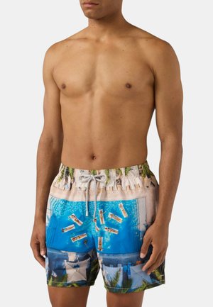 Uomo che indossa pantaloncini da bagno con una stampa colorata di persone che si rilassano su gonfiabili in una piscina e nello scenario della spiaggia circostante.
