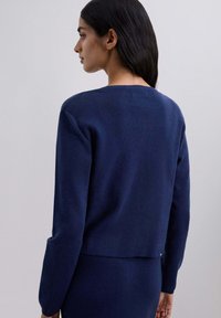 Suéter de punto azul marino con cuello redondo, mangas largas y un reverso ligeramente recortado. Textura suave y diseño simple. Sin patrones visibles.