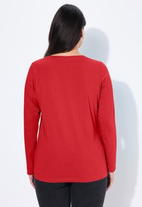Červená dlouhá rukávová košile vyrobená z měkké tkaniny, s kulatým výstřihem a uvolněným střihem. Elegantní design bez viditelných vzorů nebo akcentů.