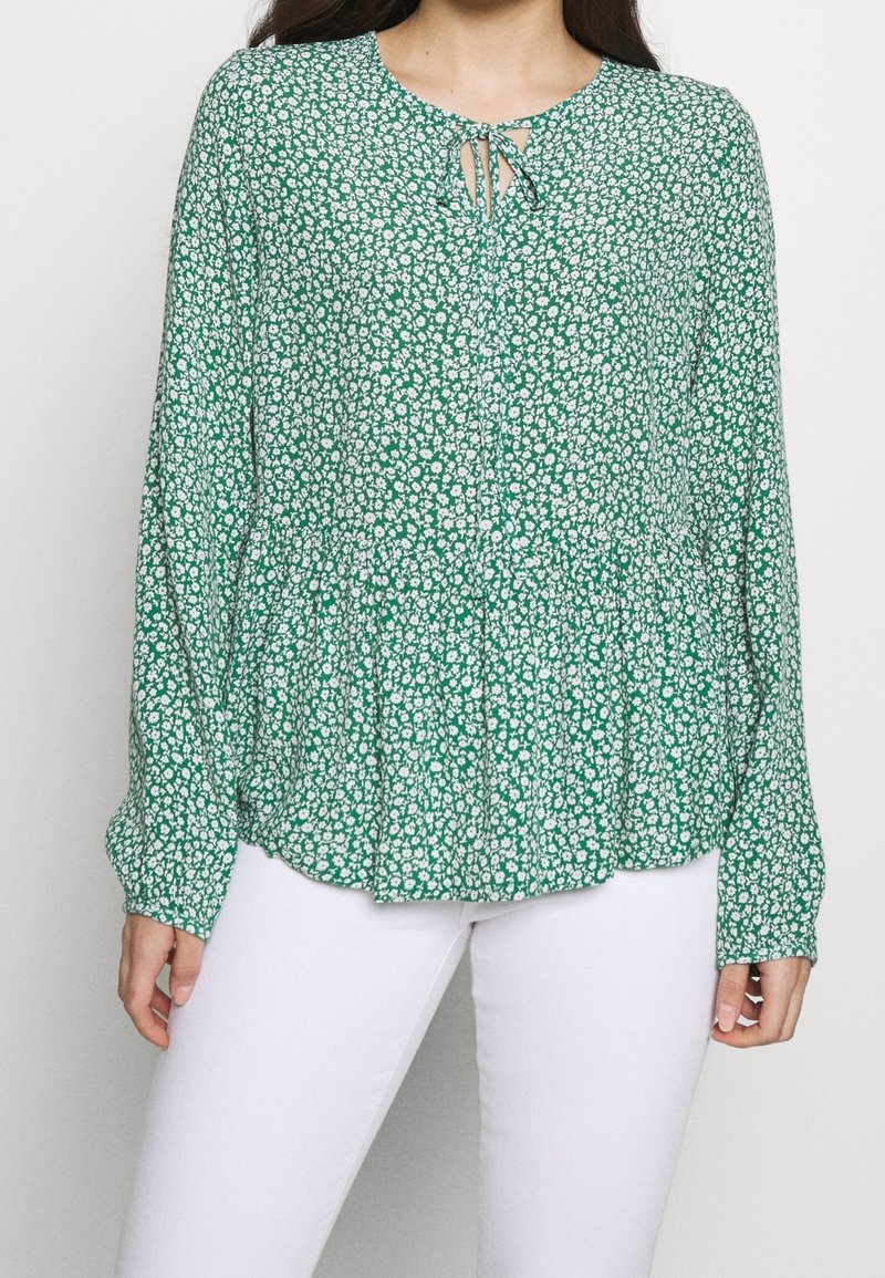 Blusa floreale verde con maniche lunghe, vita arricciata e dettaglio a chiave sul collo. Realizzata in tessuto leggero con piccoli fiori bianchi.