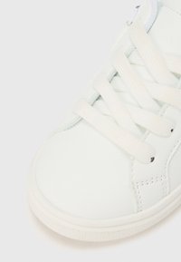 Pantof sport alb din piele, cu șireturi plate, textură netedă, vârf rotunjit și detalii subtile de cusături de-a lungul părților laterale. Talpă moale din cauciuc.