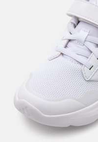Baskets blanches de sport avec une tige en mesh texturé, un design sans couture, un col rembourré et une bride auto-agrippante pour un maintien sécurisé.