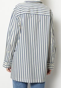 Striped shirt in cream and navy blue, featuring a collared neckline, long sleeves, and buttoned cuffs. The fabric appears smooth and lightweight.