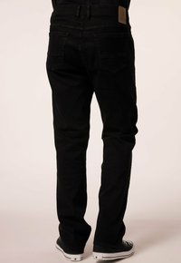 Černé džínové kalhoty s rovný střih, s zadními kapsami, koženou nášivkou na pase, a kombinované s černobílými teniskami.