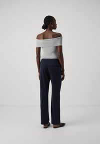 Grijs off-shoulder geribd topje gecombineerd met marineblauwe high-waisted broek met een gladde textuur en een achterzakdetail. Zwarte instapschoenen.