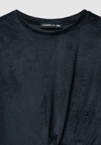 Czarny prążkowany top z okrągłym dekoltem i detalem w postaci węzła z przodu. Wykonany z miękkiego materiału, o teksturowanej powierzchni.