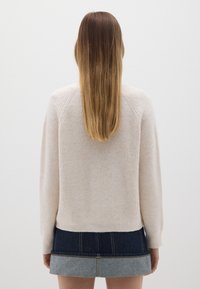 Hellbeige, gerippter Strickpullover mit langen Ärmeln, rundem Ausschnitt und lockerem Schnitt. Kombiniert mit einem Jeansrock mit hellblauem Saum.