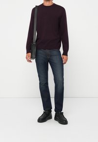 Tummanliila pyöreäkauluksinen neule, siniset farkut ja mustat lenkkitossut. Vasemman olkapään yli heitetty musta olkalaukku. Rentoa istuvuutta.