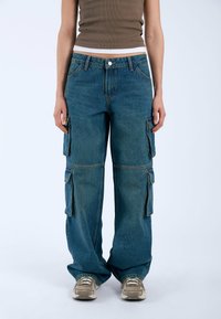 Pantalones cargo de mezclilla con un ajuste relajado, que presentan múltiples bolsillos laterales, cierre de botón y costuras visibles en amarillo contrastante.