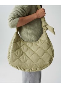 Borsa a spalla verde trapuntata con forma curvilinea e tracolla annodata, dotata di una superficie strutturata e fondo arrotondato.