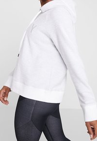 Ljusgrå hoodie med strukturerat tyg, vita dragsnören och vit nederkant. Kombination med svarta leggings med geometriskt mönster.