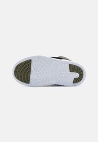 Sneaker sole with white rubber, textured surface, green accents, and a circular logo design. Flat, rounded toe with patterned tread for grip.