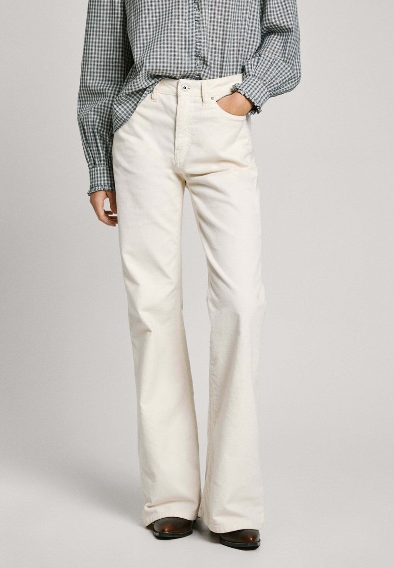 Jeans acampanados blancos hechos de algodón resistente, con cintura alta, bolsillos delanteros y una textura suave, combinados con una camisa de cuadros.