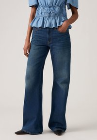 Τζιν παντελόνι με φαρδιά μπατζάκια σε μπλε χρώμα και μεσαία μέση. Διαθέτει κλασικές ραφές και σχέδιο με πέντε τσέπες. Υποτονική ξεθωριάδα στο μπροστινό μέρος.