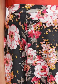 Gonna floreale con base nera, decorata con grandi fiori bianchi e rosa. Realizzata in tessuto con una texture liscia e una vita aderente.