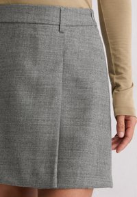 Szara, dopasowana spódnica z teksturowanej tkaniny, z płaskim przodem i subtelnym wzorem w kratę. Zbliżenie pokazuje pas oraz umiejscowienie dłoni.