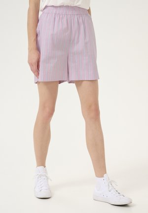 Shorts rose clair avec des rayures verticales bleues, fabriqués en tissu doux. Comprend une ceinture élastique et des poches latérales. Associés à des baskets blanches.
