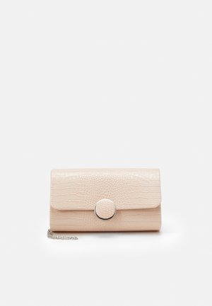 Pochette beige à motif crocodile avec fermoir rond argenté et une courte chaîne argentée sur fond blanc.