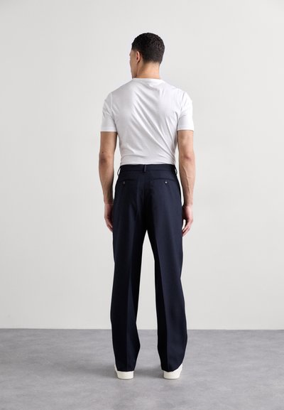 Pantalon navy à coupe ajustée, en tissu lisse, avec deux poches arrière et passants de ceinture, associé à un T-shirt blanc uni.