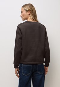 Brauner Sweatshirt mit Rundhalsausschnitt und langen Ärmeln, mit einer glatten, strukturierten Oberfläche. Getragen mit dunkelbeigen Jeans.