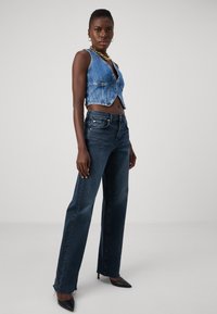 Lett blå denim cropped vest med rå kant, kombinert med høyhælte mørkeblå jeans med frynsete kanter og klassisk fem-lommers design.