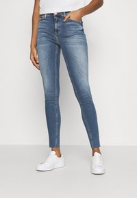 Vaqueros de denim azul ajustados con cintura alta, diseño de cinco bolsillos y dobladillo sin rematar. Combinados con zapatillas blancas para un look casual.