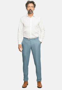 Pantalones ajustados de color azul claro con una textura sutil, combinados con una camisa blanca de manga larga. Zapatos de vestir marrones completan el atuendo.