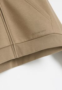 Beżowy sweatshirt z prążkowanymi mankietami i dołem, z delikatnym przeszyciem oraz małym haftowanym logo "diverse" z przodu.