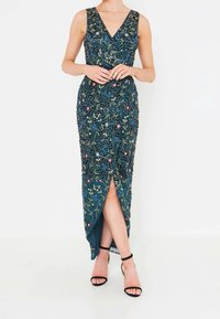 Long, teal evening dress with beaded floral patterns, v-neckline, and side slit. Styled with black strappy heels.