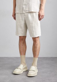 Pantaloni corti in lino di un beige chiaro, con una vestibilità rilassata e tasche laterali. Abbinati a calzini beige e mocassini color crema con una suola testurizzata.