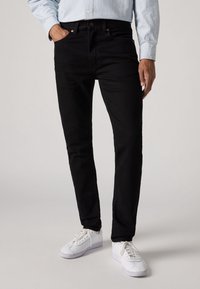 Svarta jeans i denim med smal passform, sidfickor och minimalistisk design, kombinerade med vita sneakers.