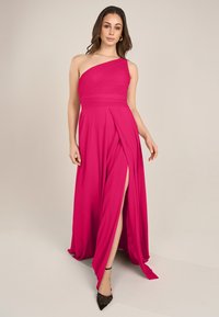 Fuchsia-einseitiges Kleid aus leichtem Stoff mit gefaltetem Oberteil, Schlitz bis zum Oberschenkel und fließendem Rock. Kombiniert mit schwarzen spitzen Absatzschuhen.