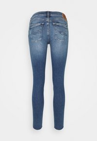 Skinny jeans in faded blue denim with a smooth texture, featuring two back pockets and a brown leather patch at the waistband.
