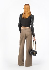 Zkrácená černá bunda s koženými rukávy, spárovaná s taupe kalhotami s širokými nohavicemi. Drží černou kabelku se zlatými detaily.