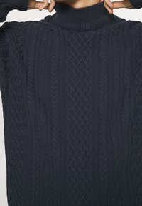 Maglione a collo alto blu navy lavorato a maglia con un motivo a trecce testurizzato, dettagli a coste e una vestibilità comoda.