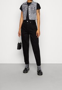 Chaleco recortado a cuadros blanco y negro sobre una camiseta negra, combinado con pantalones negros de cintura alta y botas negro con cordones. Pequeño bolso.