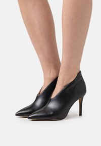 Black leather high-heeled shoes with a pointed toe, sleek design, and side cutouts, featuring a slender heel and smooth texture.