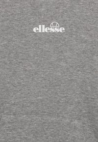 Sweatshirt gris en tissu doux et texturé, avec un logo "ellesse" blanc centré en haut. Comprend une poche kangourou.