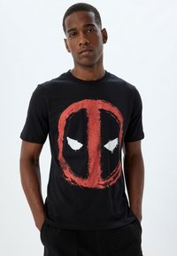 Sort bomulds t-shirt med en rød og hvid grafik af en maske på forsiden. Kortærmet og med rund halsudskæring.