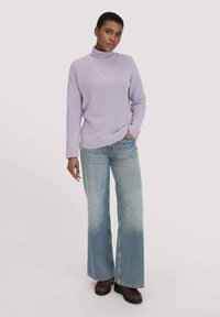 Lila gebreide trui met een v-hals en lange mouwen, gedragen over een lichtere coltrui; gecombineerd met flared lichtblauwe jeans en donkere schoenen.