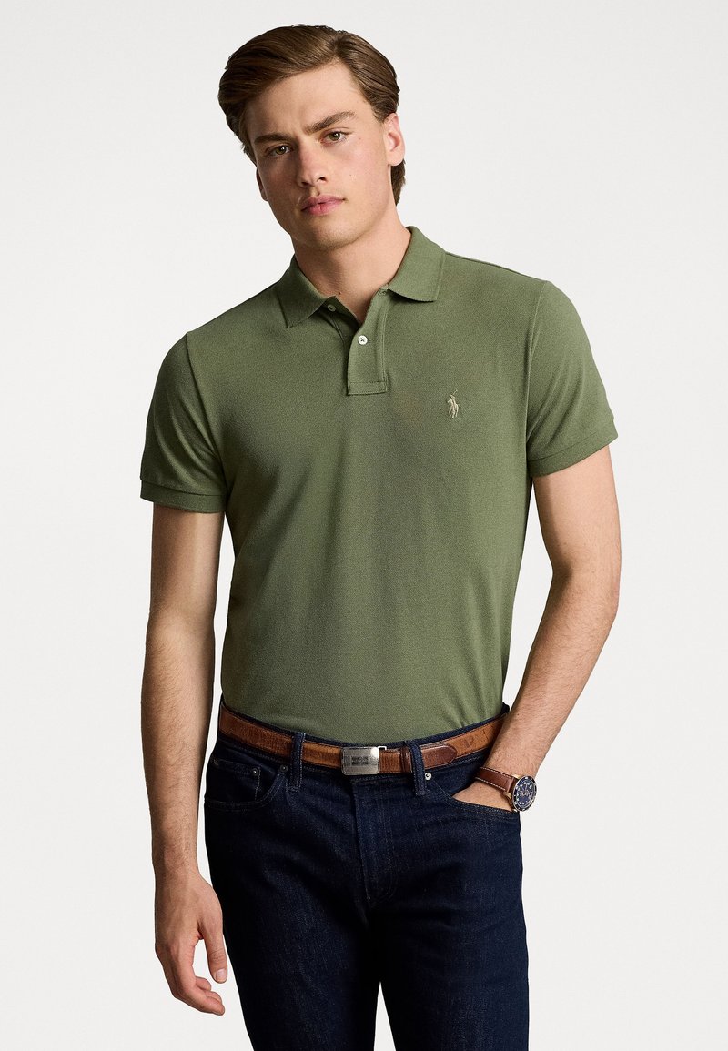 Tricou polo verde cu gât căptușit, mâneci scurte și un logo pe piept. Asortat cu blugi denim închiși la culoare și o curea maro.